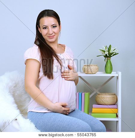 Young regnant woman sitting on armchair on wall background