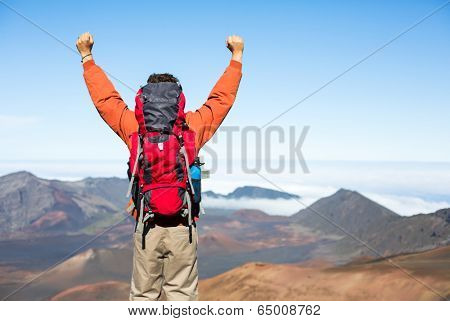 Hiker with backpack enjoying view from top of a mountain. Celebrating victory making it to the summit. Success and achievement concept.