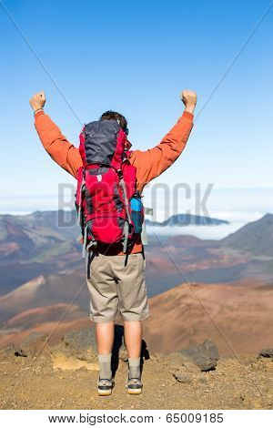 Hiker with backpack enjoying view from top of a mountain. Celebrating victory making it to the summit. Success and achievement concept.