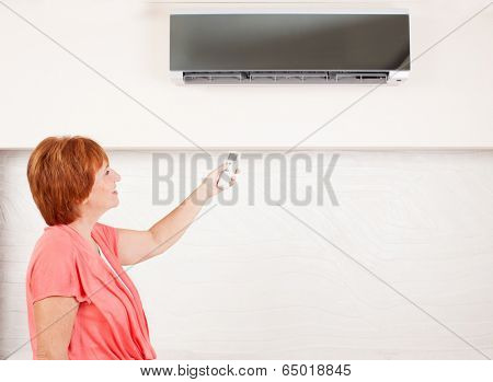 Woman holding a remote control air conditioner at home. Happy mature woman on sofa