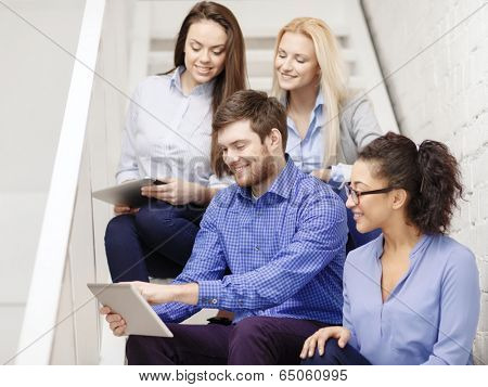 business, technology and startup concept - smiling creative team with tablet pc computer sitting on staircase
