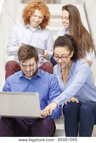 business, technology and startup concept - smiling creative team with laptop and tablet pc computer sitting on staircase
