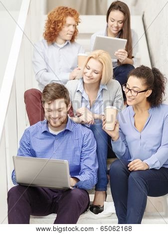 business, technology and startup concept - smiling creative team with laptop and tablet pc computer sitting on staircase