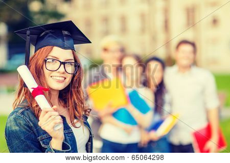 education, campus and teenage concept - smiling teenage girl in corner-cap and eyeglasses with diploma and classmates on the back