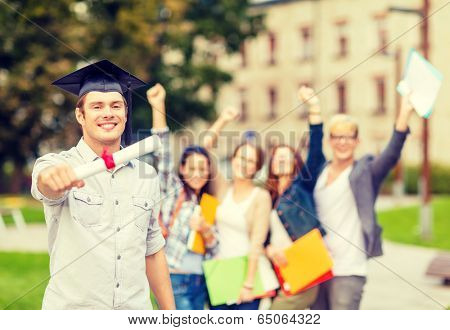 education, campus and teenage concept - smiling teenage boy in corner-cap with diploma and classmates on the back