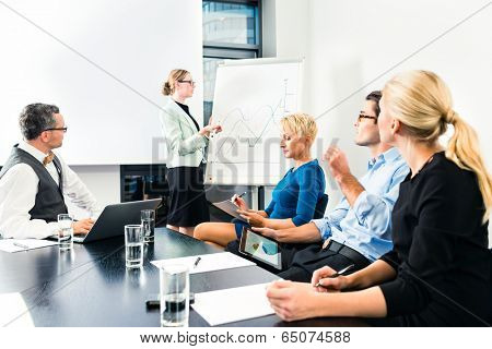 Business - presentation within a team, a female colleague is standing on the flipchart and explaining the development
