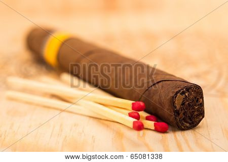 One cigar and five matches with red heads on a wooden surface