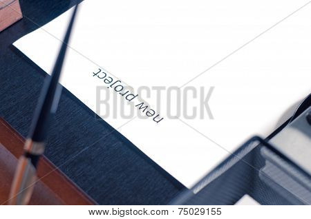 Sheet Of Paper On A Table With The Word New Project. Insert Your Text