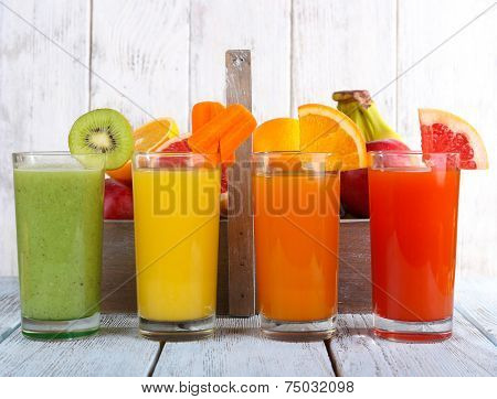 Fruit and vegetable juice in glasses and fresh fruits in box on wooden table on wooden wall background