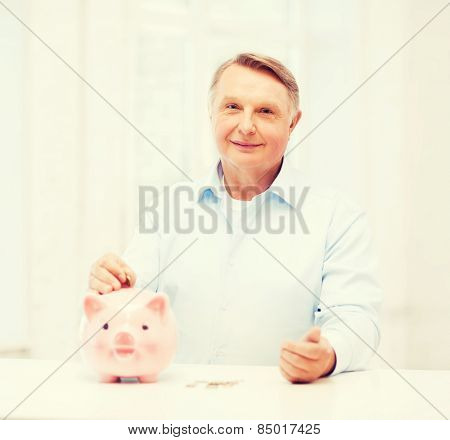savings, oldness,business and banking concept - old man putting coin into big piggy bank