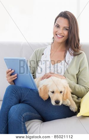 Happy beautiful woman with dog using tablet computer on sofa at home