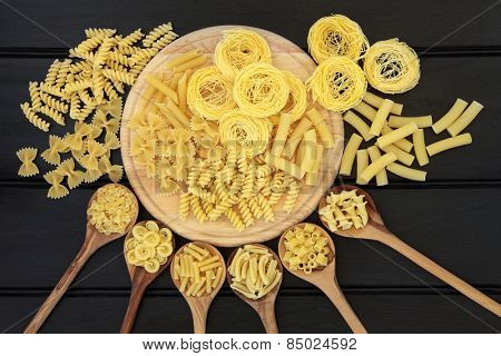 Italian dried food selection on a wooden board and in olive wood spoons over dark wood background.