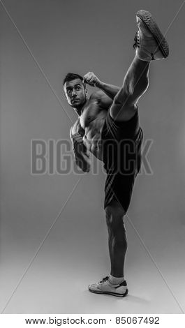 Portrait of a muscular man practicing body combat over gray background. HDR monochrome