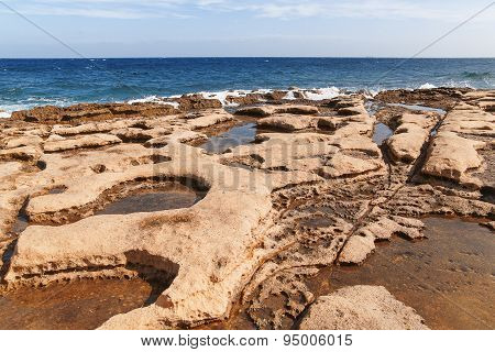 The Waves Beat Against The Rocky Shore. Water Flooded Depressions In The Rocks. Malta, Saint Julians