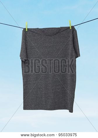 Close Up Of A Dark Grey T-shirts On The Rope. Cloudy Sky Background.