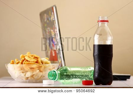 Bottles of softdrinks or soda, chips and a laptop computer in the background