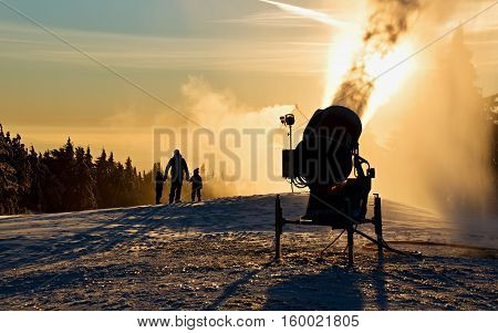 Father is playing with his children next to the snow cannon.