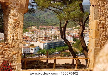 Aerial view from old arch of European town on a natural hills with many bars hotels and restaurants in sunny day with blue sky. Tossa De Mar Costa Brava Spain.
