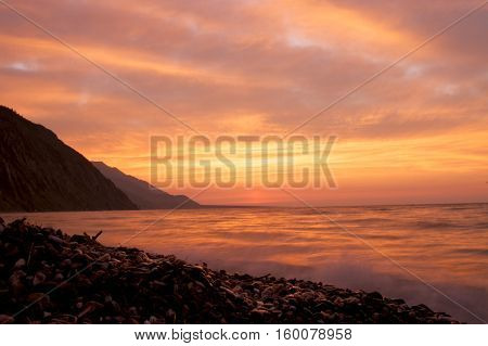 Pebble beach on the shore of Lake Baikal, the cloudy sunset sky