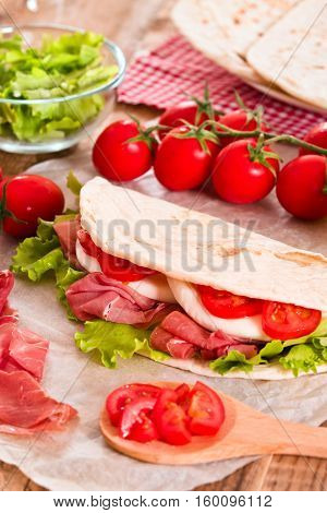 Piadina with ham and lettuce on wooden table.