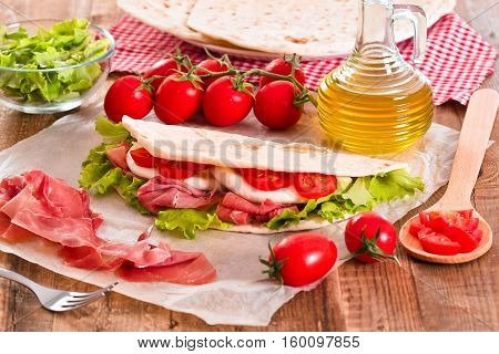 Piadina with ham and lettuce on wooden table.