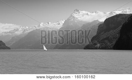 Grandiose mountain landscape. Mountain tops in the snow. Steamship floats on the lake. Black and white.