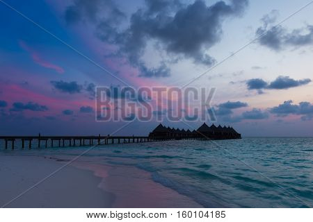 Gorgeous sunset over the ocean. Splash of waves on the white sand beach. Relaxing summer evening. Panorama of tropical island Beach with оverwater bungalows