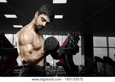 Muscular athletic bodybuilder fitness model posing after exercises in gym