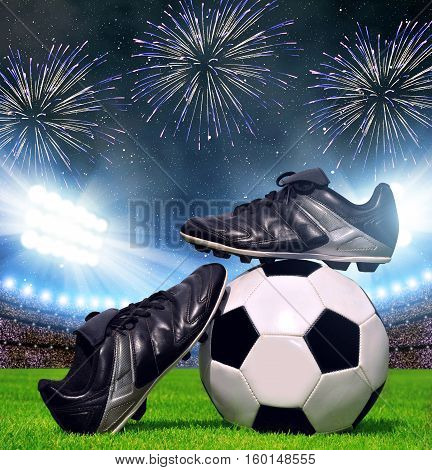 Soccer ball and shoes in grass, football stadium with the dright lights.