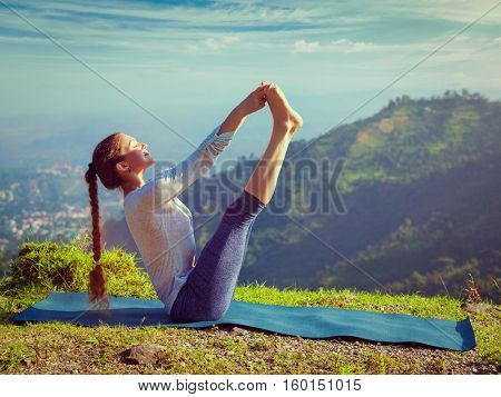 Yoga outdoors - woman doing Ashtanga Vinyasa Yoga balance asana Ubhaya padangusthasana Big Double Toe Yoga Pose in Himalayas in India in the morning. Vintage retro effect filtered hipster style image.