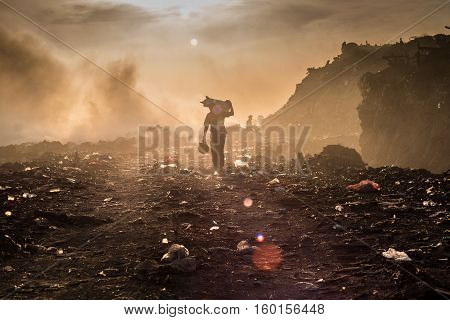 A waste picker is collecting reusable or recyclable materials in a open burning dump.