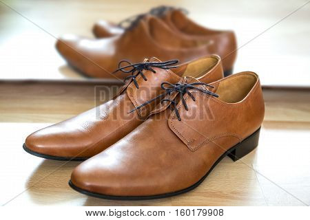 Classic brown lace up leather male dress shoes placed next to the mirror on a wooden floor. Timeless oxford desing smooth toe fine stitching all-leather construction