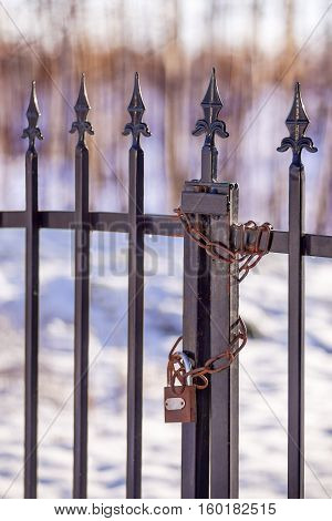 Old rusty padlock with rusty chain on a metallic fence in winter