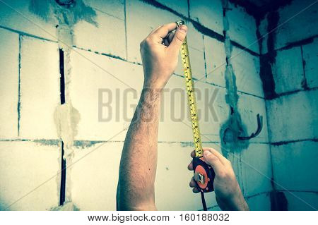 Worker with yellow tape measure in centimeters and feets measure the distance to the newly built walls from bricks - retro style