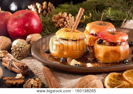 Baked apples on brown plate with holiday Christmas decoration with Christmas tree branch cones cinnamon walnuts and red apple.