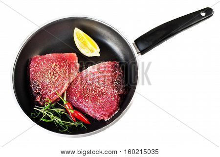 Raw fresh tuna fillet with herbs salt and lemon in a frying pan isolated on white background. Tuna steak