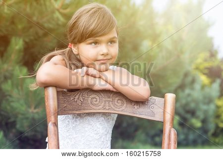 Portrait of long haired brunette little girl leaning on an vintage wooden chair. The sunlight is in the upper right side of the photo.