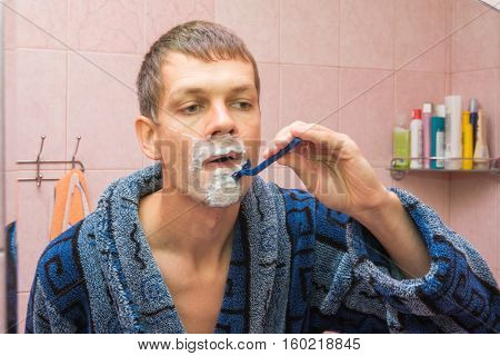 Young Man Shaving In Front Of Mirro