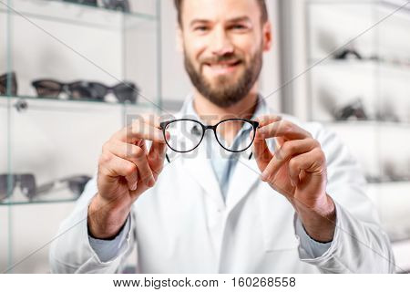 Handsome ophthalmologist holding eyeglasses for a try out. Optometrist offering to wear a pair of glasses. Image with small deph of field focused on the hands and glasses
