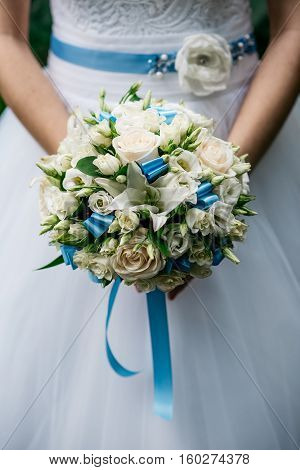 Cropped image. The bride holds a wedding bouquet of white roses and blue satin ribbons