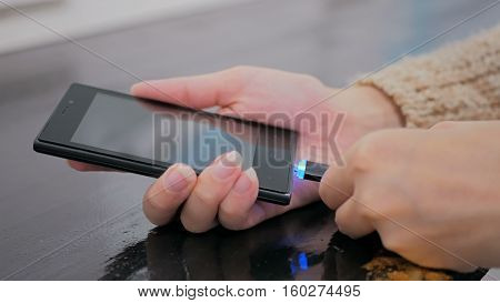 Woman's hand plugging black lightning charging cable into smartphone - USB data cable connecting on modern gadget. Close up