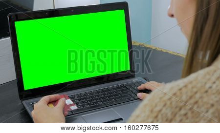 Young woman buying goods from the internet and entering number security code from credit card on laptop with green screen. Online, technology and internet concept.