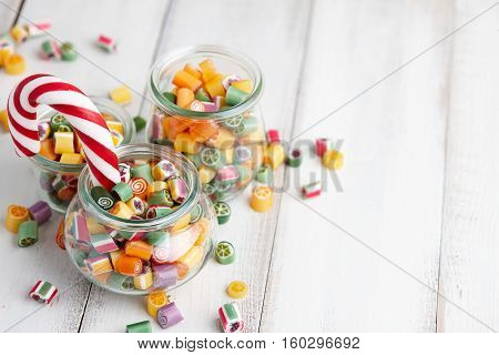 Colorful lollipops and candy canes in glass jars on white wooden background