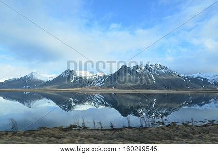 Beautifu snow covered mountains in Iceland reflecting in a pool of water.
