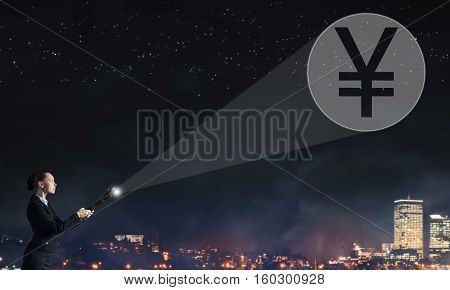 Young elegant businesswoman with flashlight in darkness and yen currency symbol