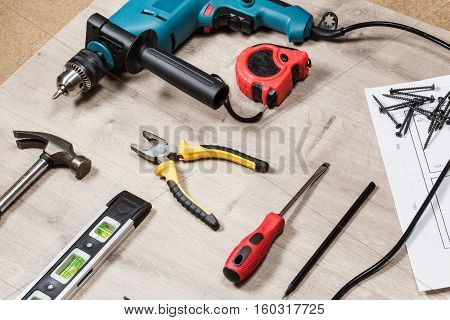 Set of construction tools to repair on a wooden surface: drill, hammer, pliers, self-tapping screws, roulette, construction level, drawing, construction pencil. Side view