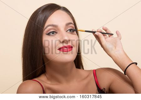 Young model woman usikng pencip for doing makeup isolated on white. Pretty lady paiting her eyes for photosession. Cosmetics concept.
