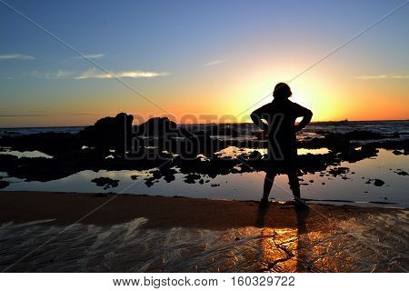 Sihouette of a teenage boy facing the ocean at sunset