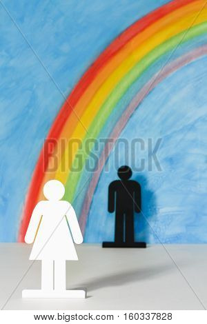 Man and women icons with a rainbow and blue sky to illustrate the concept of male female and sexual discrimination; woman in foreground.