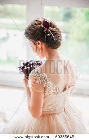 Beautiful charming bride in a luxurious dress looking up.Portrait Of Happy Bride Sitting in wedding dress in a white photo Studio. Young attractive bride with flowers